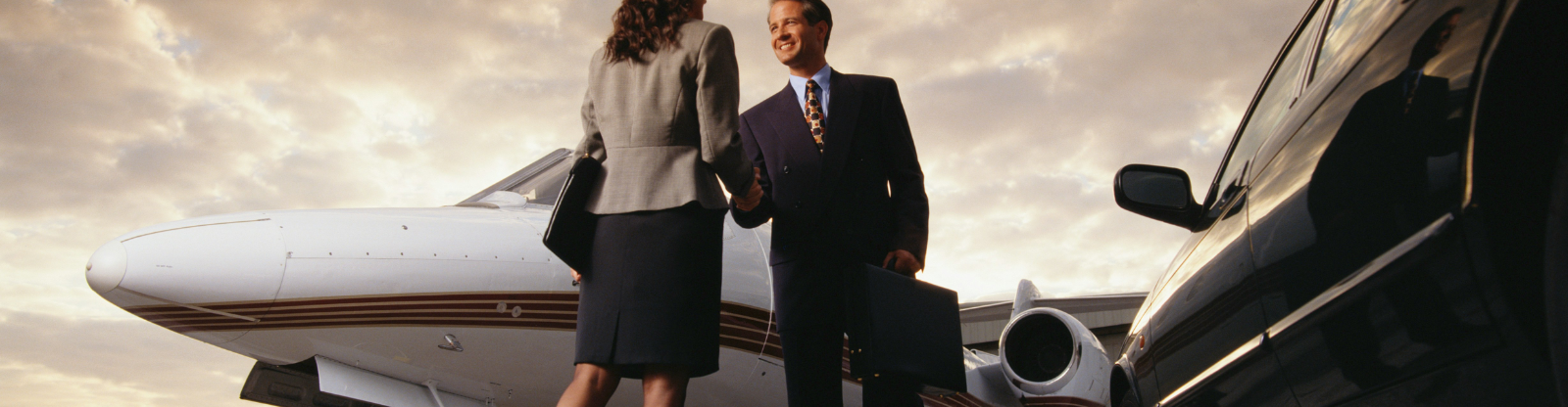 JetTarmac+Car_1600x900px_Man+WomenBusiness business man and business woman on tarmac entering a private jet